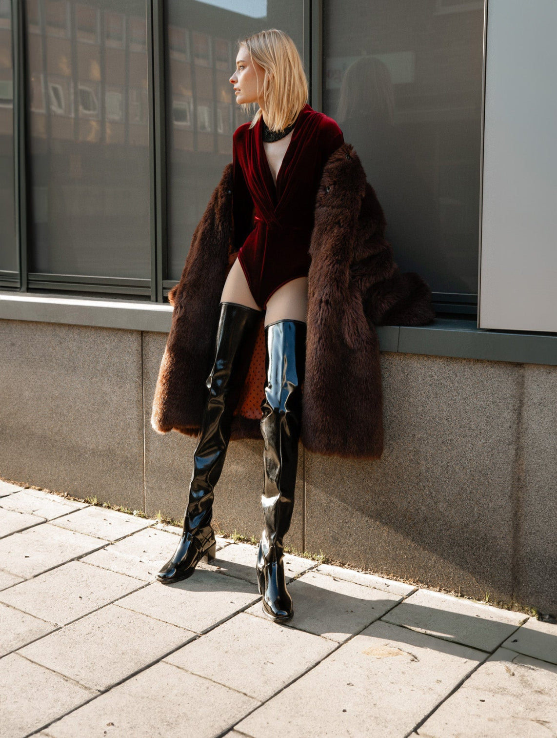 Stylish woman in ACQUO of Sweden’s signature over-the-knee boots, paired with a burgundy velvet bodysuit and a luxurious faux fur coat—an elegant fusion of Scandinavian fashion and confident city edge