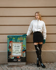 Model wearing ACQUO of Sweden over-the-knee glowing black boots, paired with a black mini skirt, cream bomber jacket, and teal gloves – striking urban fashion captured against a beige wall and colorful street art panel