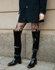Close-up of a stylish outfit featuring ACQUO of Sweden’s signature black over the knee rubber boots, paired with sheer floral patterned tights and a pinstripe blazer dress—capturing contemporary Scandinavian fashion with a bold and elegant street style edge