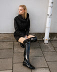 Model styled in ACQUO of Sweden’s sleek over-the-knee black patent boots with flat sole, matched with a cinched black utility jacket – a striking and contemporary street style look with minimalist edge