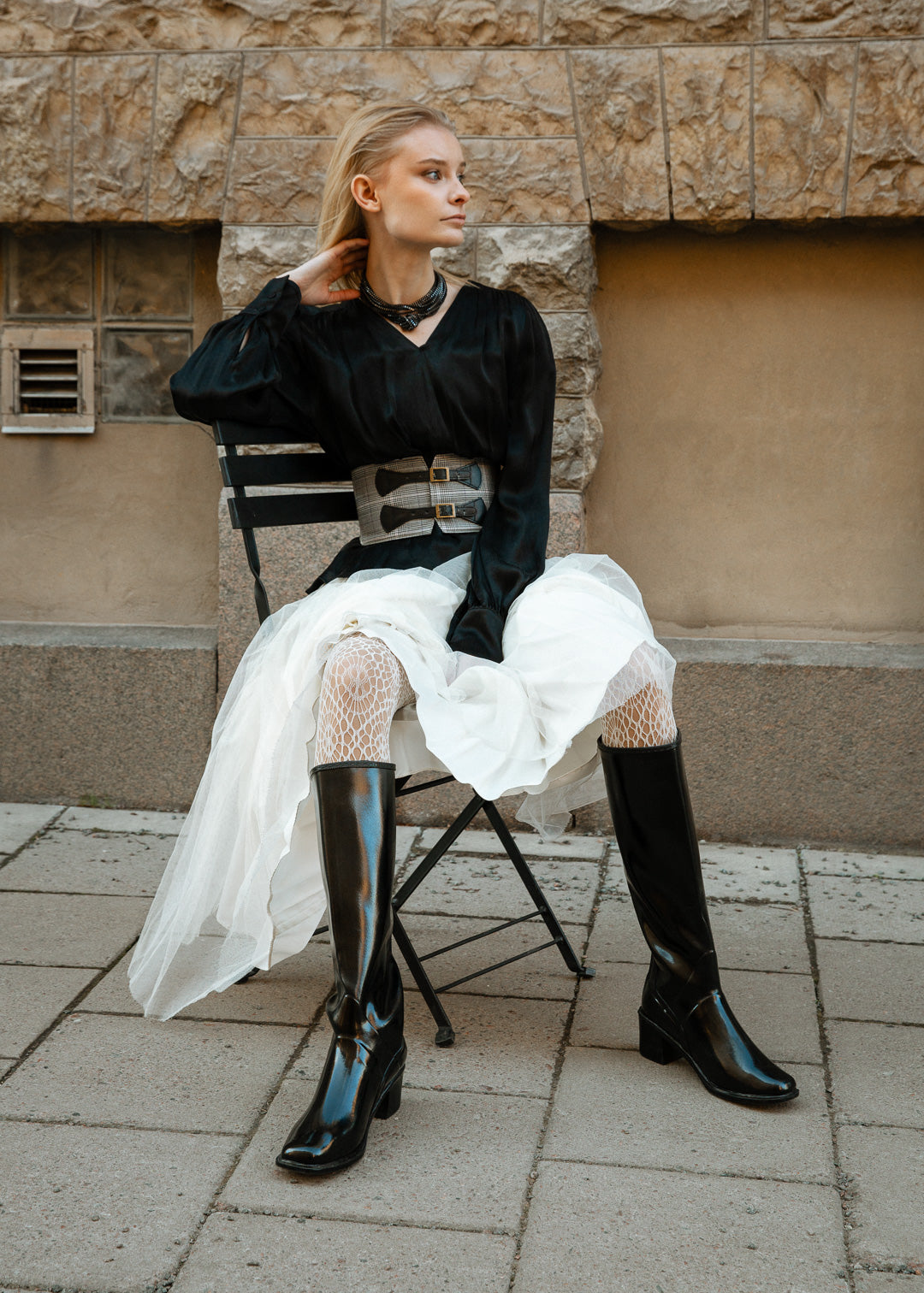 Model in ACQUO of Sweden's knee-high sleek shine black boots with a block heel, paired with a flowing white tulle skirt, textured white tights, and a sleek black blouse – blending feminine elegance with edgy street style