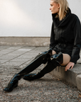 Model in urban street setting wearing ACQUO of Sweden’s black over the knee rubber boots and edgy black zippered jacket, showcasing minimalist Swedish design and fashion-forward footwear perfect for modern style lovers.