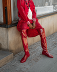 Model wearing Greta Cherry Red over-the-knee boots by ACQUO of Sweden styled with a red skirt and satin bomber jacket in an urban setting. Waterproof boots with elegant Swedish design and modern Scandinavian fashion appeal.