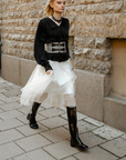 Fashionable woman walking in the city wearing ACQUO of Sweden black natural rubber boots styled with a white tulle skirt and black blouse.