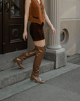 Woman walking down stone steps wearing Lisa Walnut Brown knee-high boots by ACQUO of Sweden with a brown suede outfit and statement necklace. Elegant waterproof boots with refined Swedish design styled for sophisticated city fashion.