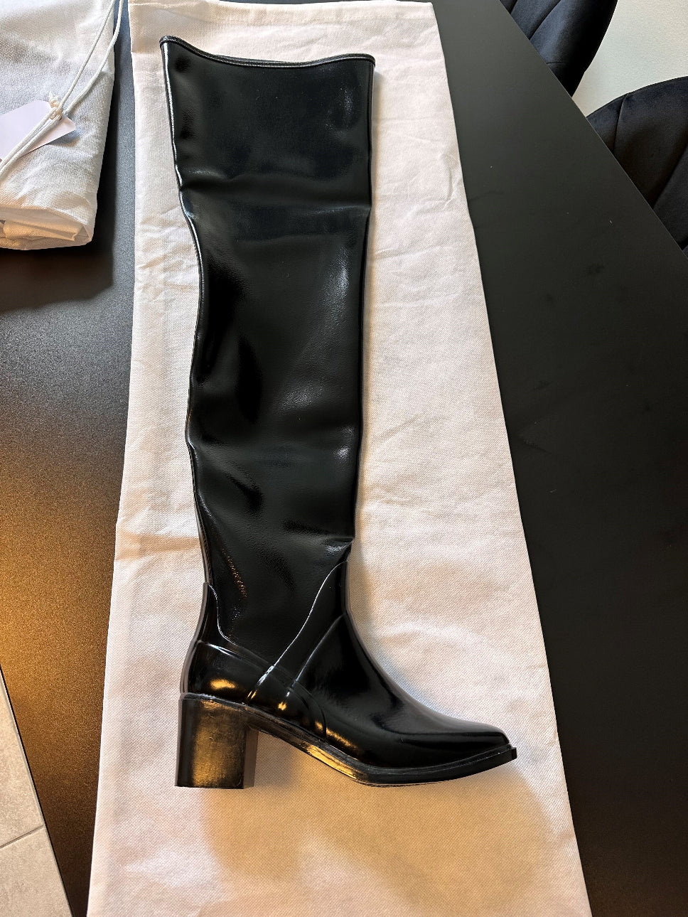 ACQUO of Sweden knee-high glossy rubber boot with mid-height block heel, elegantly displayed on a white dust bag, highlighting timeless Swedish design