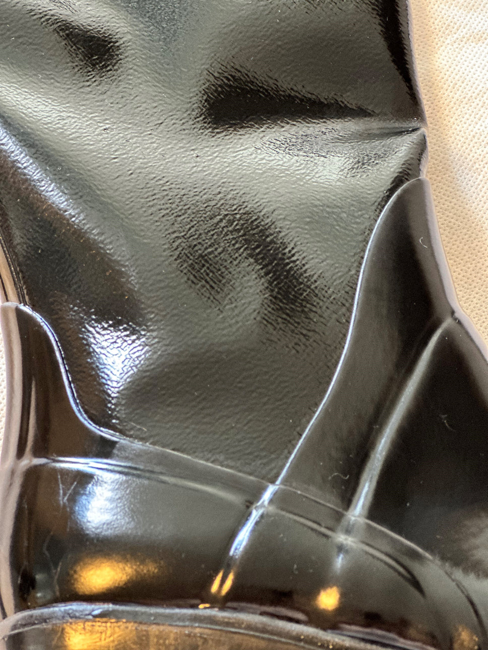 Macro shot of ACQUO of Sweden's black rubber boot, showcasing the detailed grain, high-shine surface, and precise panel craftsmanship of the premium fashion boot."