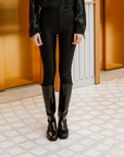 Front view of ACQUO of Sweden's sleek knee-high black rubber boots styled with fitted black trousers and a satin blouse—timeless Scandinavian craftsmanship meets contemporary fashion
