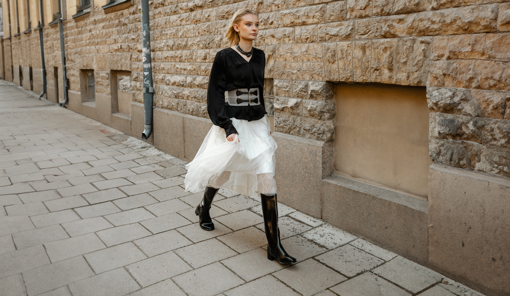 Fashionable woman walking in the city wearing ACQUO of Sweden black natural rubber boots styled with a white tulle skirt and black blouse.
