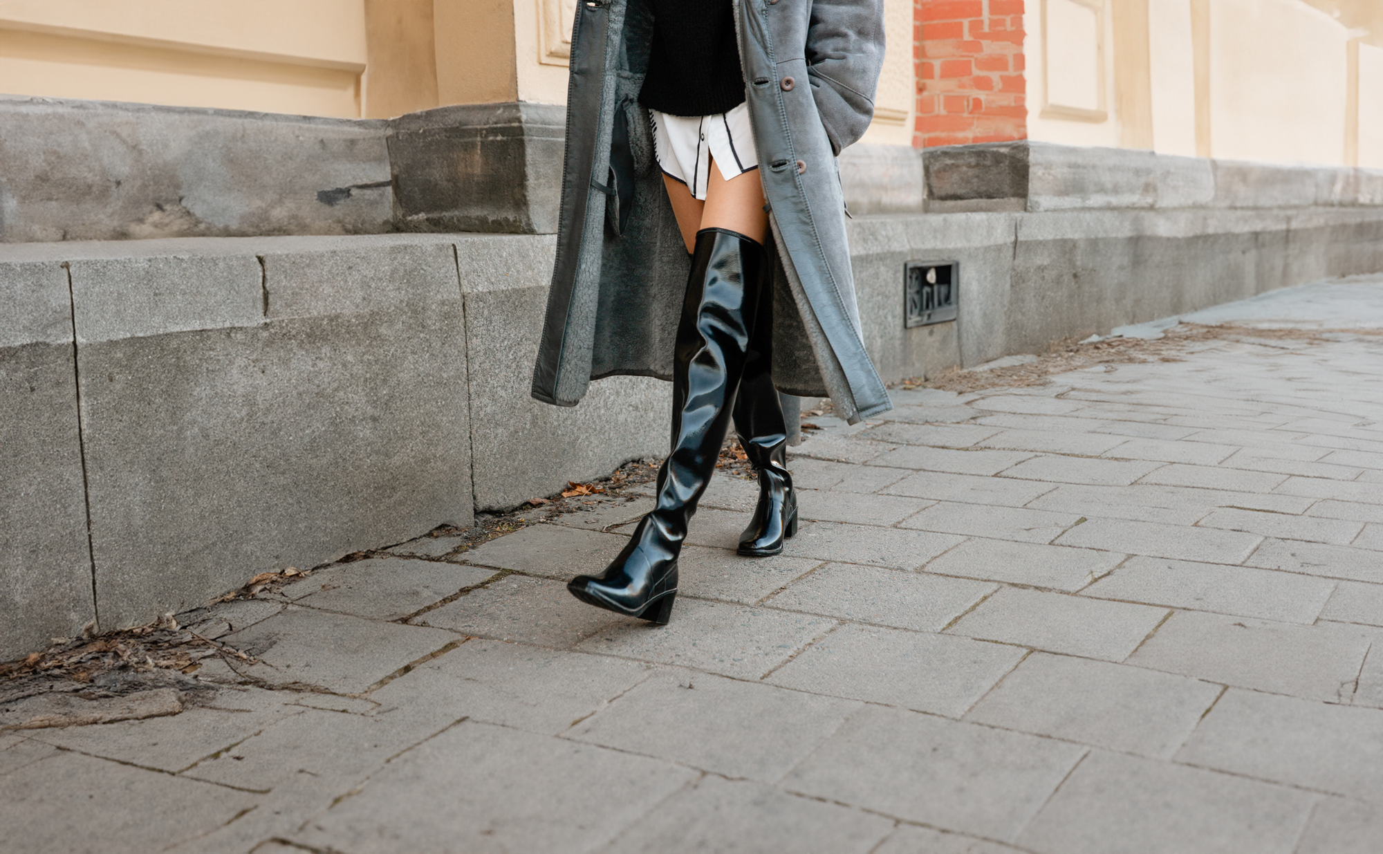 Close-up street style of ACQUO of Sweden over-the-knee boots made from black natural rubber, styled with a long grey coat