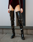 Close-up of model wearing ACQUO of Sweden over-the-knee glowing black heeled boots, styled with a deep red velvet bodysuit – a bold and luxurious fashion statement with a sleek, high-shine finish