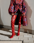 Model wearing Elsa Cherry Red over-the-knee rubber boots by ACQUO of Sweden, styled with a floral statement coat and black tights. Elegant waterproof boots with a bold silhouette inspired by contemporary Swedish design.
