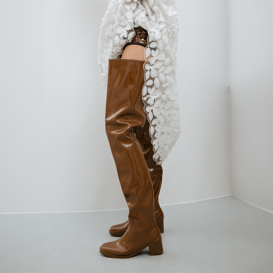Side view of Elsa Walnut Brown over-the-knee boots by ACQUO of Sweden styled with a white floral lace garment in a minimalist indoor setting. Waterproof boots with elegant Swedish design and sophisticated Scandinavian fashion details.