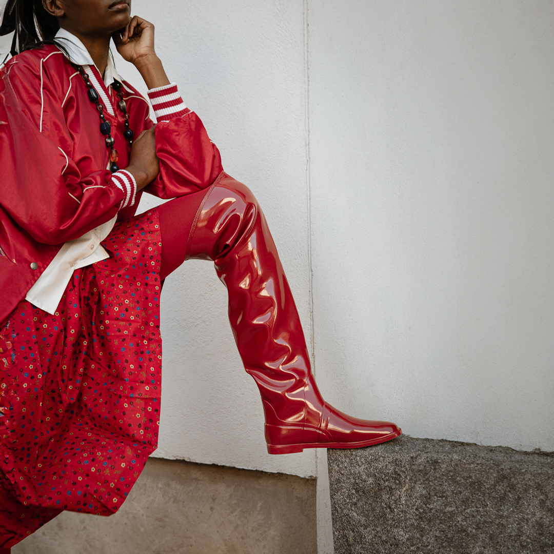 Model wearing Greta Cherry Red over-the-knee boots by ACQUO of Sweden styled with a red patterned dress and satin jacket. Waterproof boots with elegant Swedish design and contemporary Scandinavian fashion inspiration