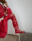 Model wearing Greta Cherry Red over-the-knee boots by ACQUO of Sweden styled with a red patterned dress and satin jacket. Waterproof boots with elegant Swedish design and contemporary Scandinavian fashion inspiration