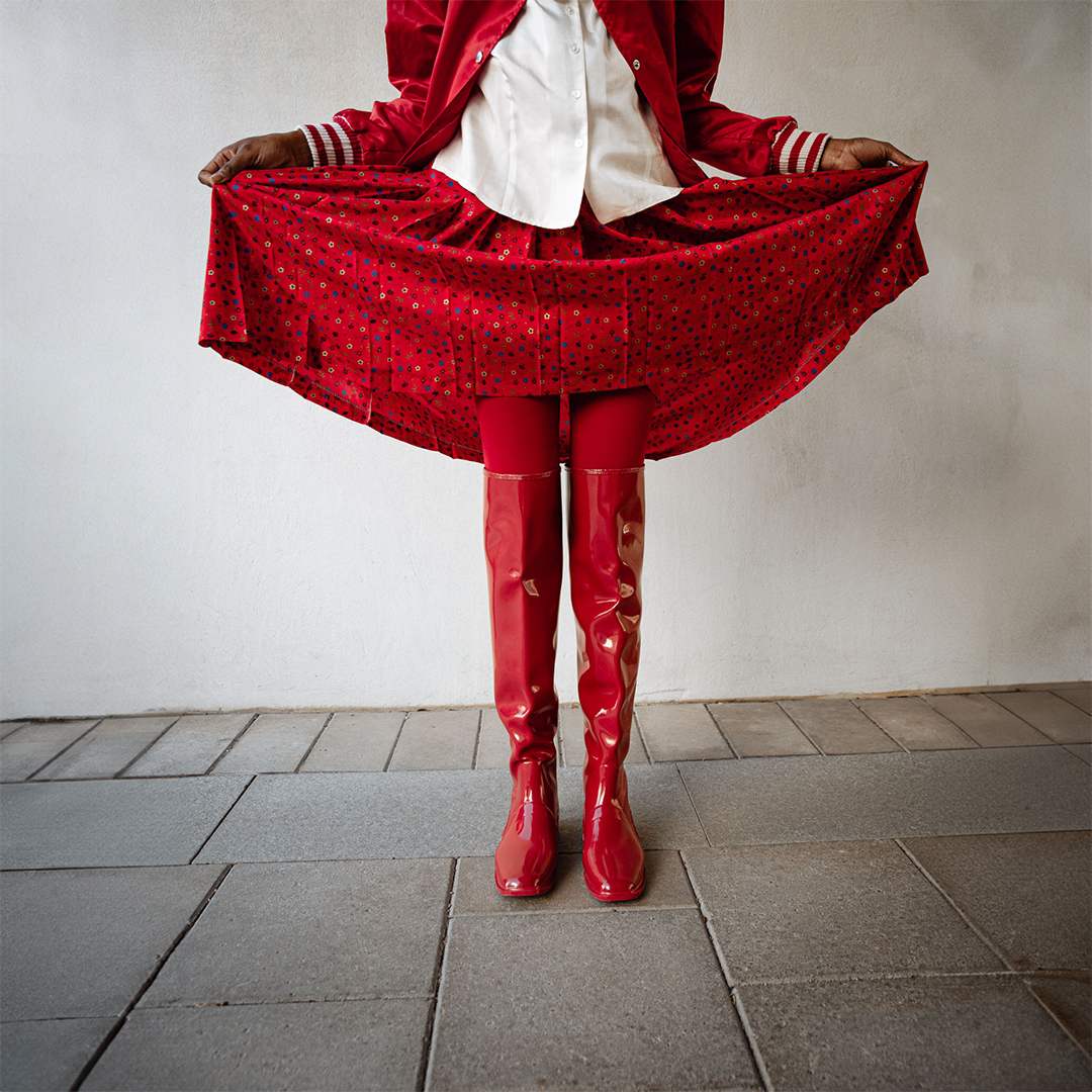 Model wearing Greta Cherry Red over-the-knee boots by ACQUO of Sweden styled with a flowing red skirt and satin jacket. Waterproof boots featuring elegant Swedish design and bold Scandinavian fashion styling
