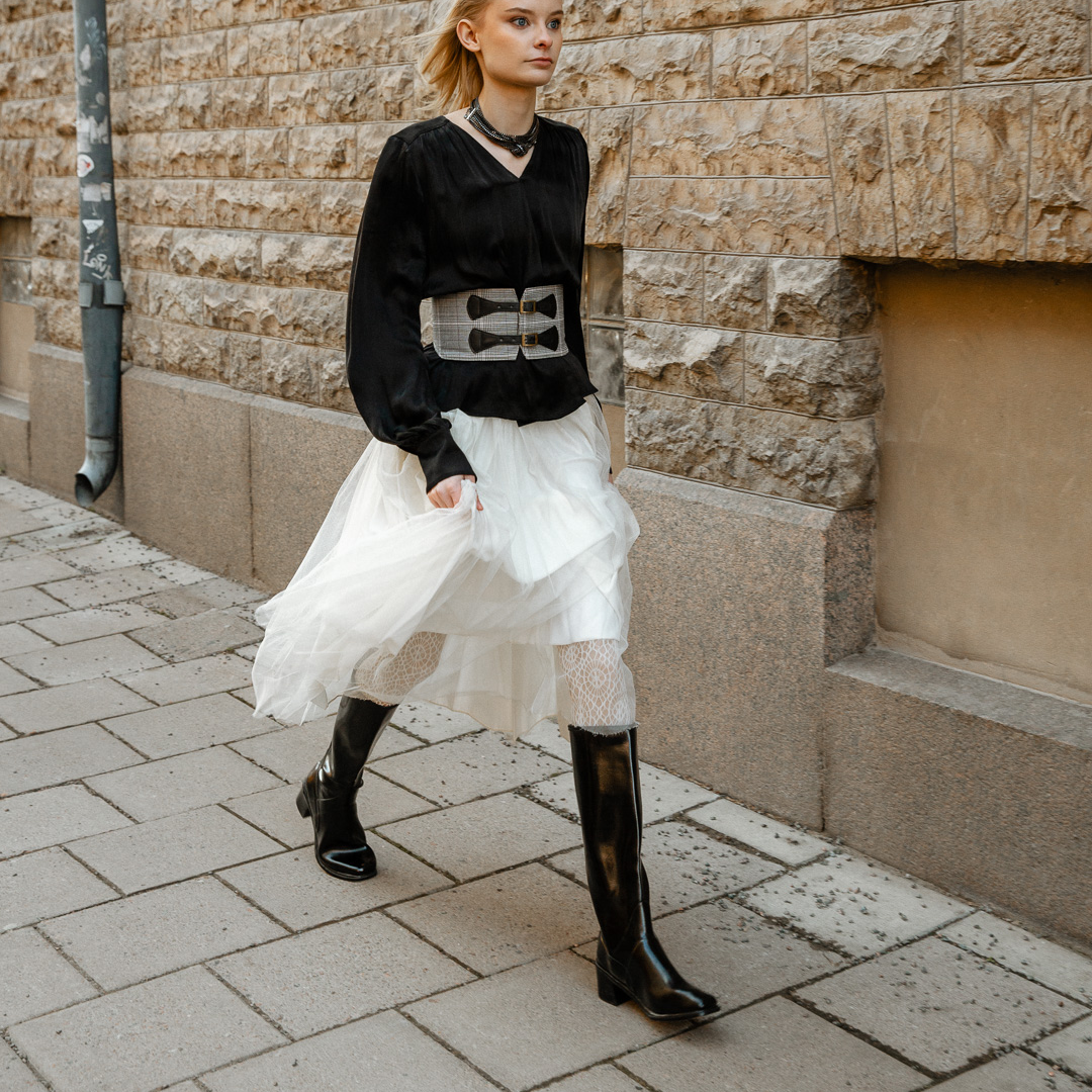 Fashionable woman walking in the city wearing ACQUO of Sweden black natural rubber boots styled with a white tulle skirt and black blouse.