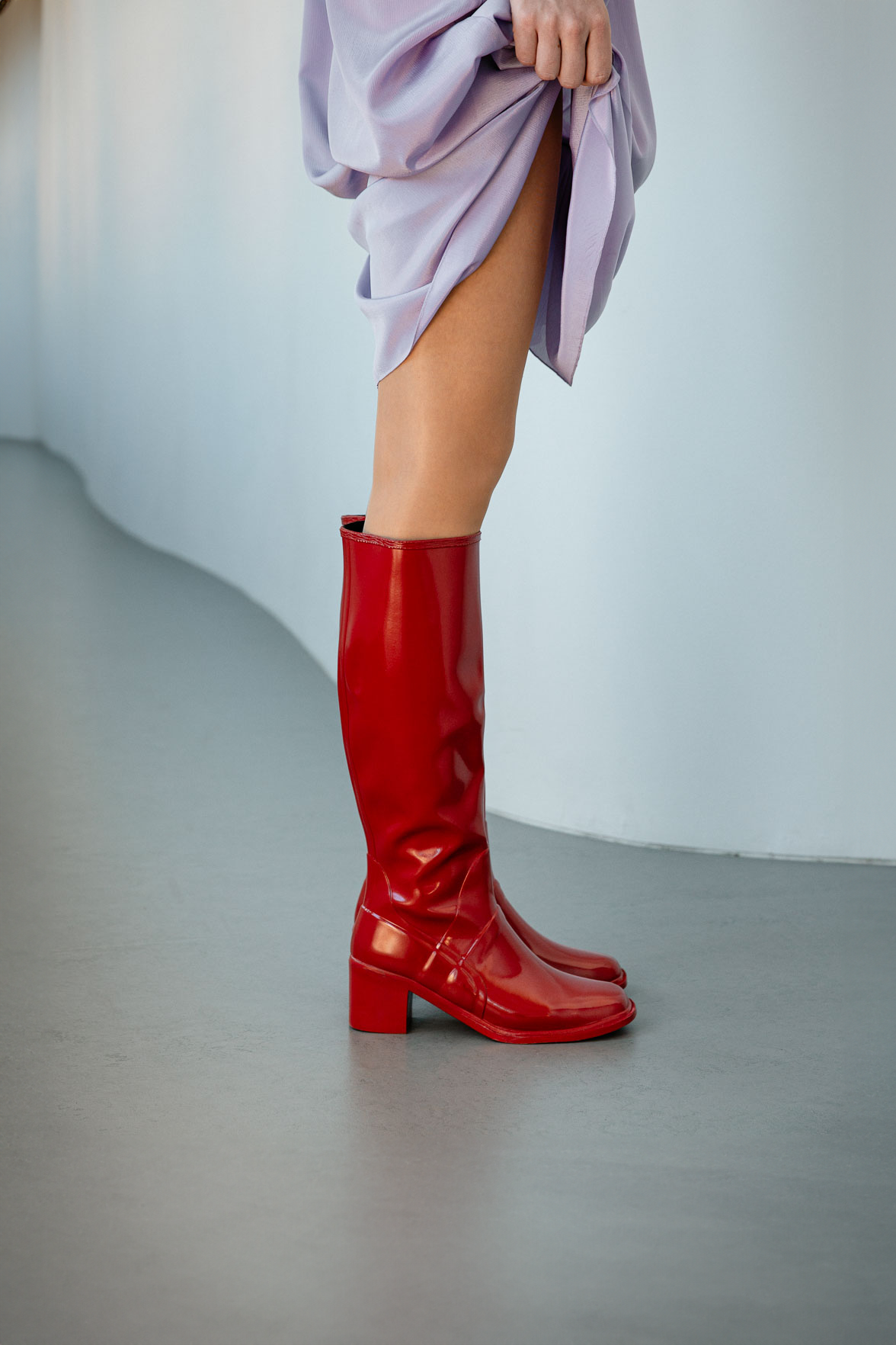 Close-up of Karin Cherry Red knee-high boots by ACQUO of Sweden styled with a lavender dress in a modern indoor setting. Waterproof boots featuring elegant Swedish design and timeless Scandinavian fashion