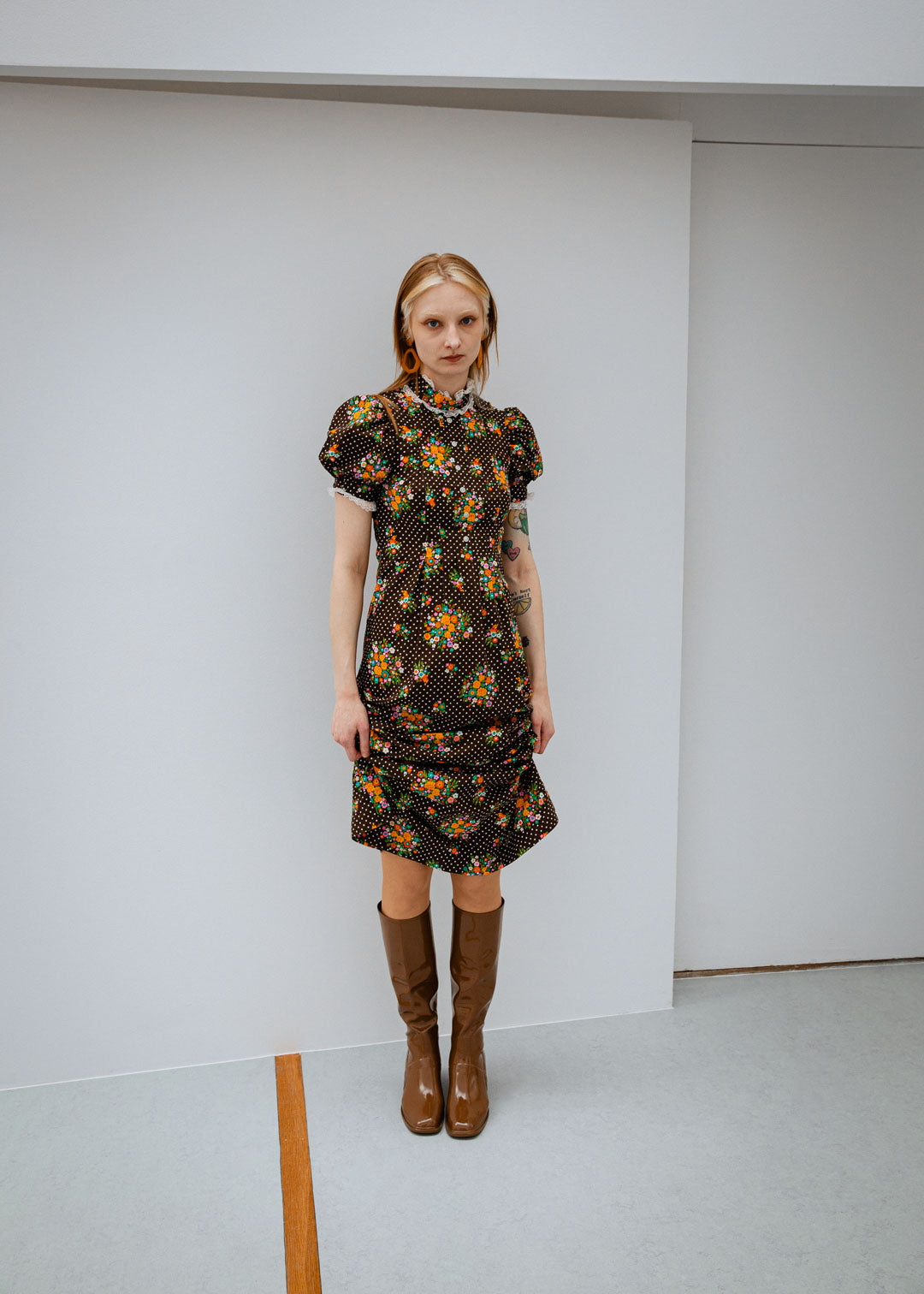 Woman wearing Karin Walnut Brown knee-high boots by ACQUO of Sweden paired with a vintage-inspired floral dress in a minimalist studio setting. Elegant waterproof boots with refined Swedish design, square toes and a timeless feminine silhouette.