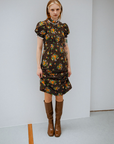 Woman wearing Karin Walnut Brown knee-high boots by ACQUO of Sweden paired with a vintage-inspired floral dress in a minimalist studio setting. Elegant waterproof boots with refined Swedish design, square toes and a timeless feminine silhouette.