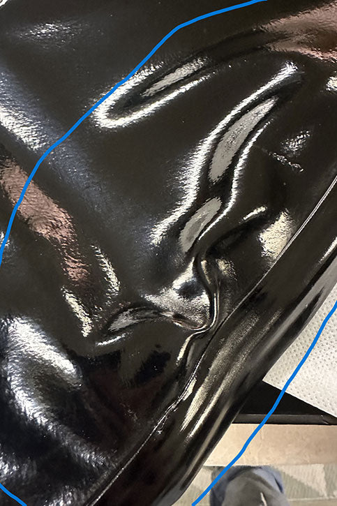 Close-up of ACQUO of Sweden black rubber boot surface with deep creases, dents, and visible wrinkles in the material.