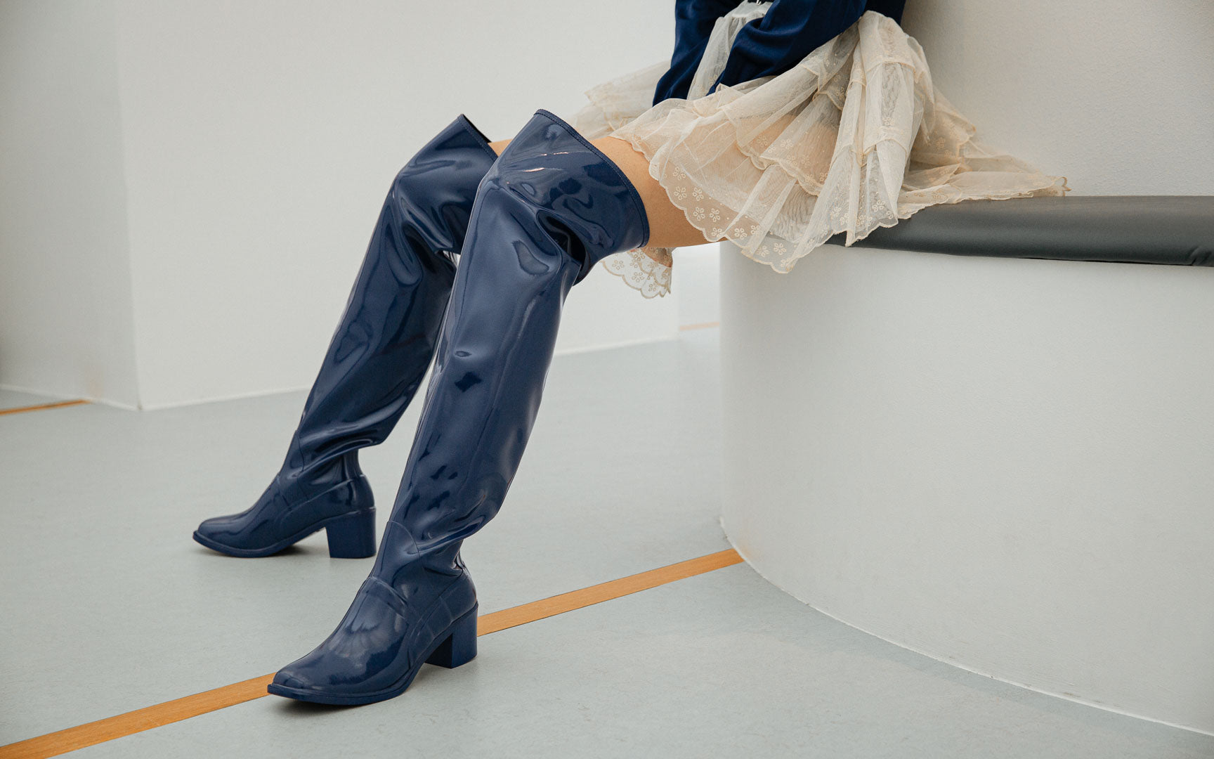 Close-up of ACQUO of Sweden Lisa Iris Blue over-the-knee natural rubber boots with a 6 cm block heel, styled with a flowing cream skirt to highlight elegant Swedish design and timeless sophistication.