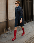 Woman walking through a city street wearing Svea Cherry Red knee-high boots by ACQUO of Sweden with a navy embroidered dress and sunglasses. Waterproof boots featuring elegant Swedish design and modern Scandinavian fashion
