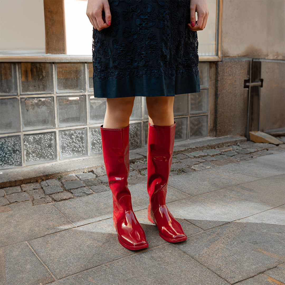 Close-up of Svea Cherry Red knee-high boots by ACQUO of Sweden styled with a navy embroidered dress on a city street. Waterproof boots with elegant Swedish design and timeless Scandinavian fashion details.