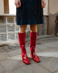 Close-up of Svea Cherry Red knee-high boots by ACQUO of Sweden styled with a navy embroidered dress on a city street. Waterproof boots with elegant Swedish design and timeless Scandinavian fashion details.