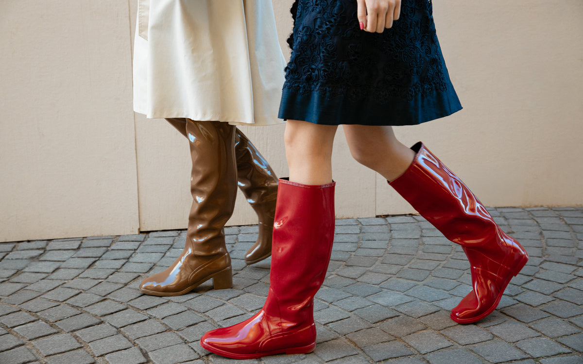 Two women walking in red and brown ACQUO of Sweden natural rubber boots, styled with dresses on a cobblestone street.