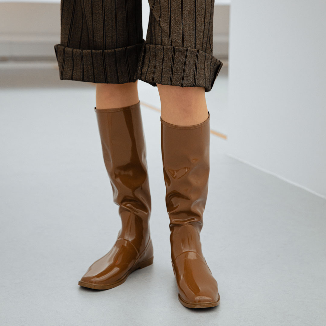Close-up of Svea Walnut Brown knee-high boots by ACQUO of Sweden paired with tailored pinstripe trousers in a minimalist studio. Elegant waterproof boots with clean Swedish design, square toes and a modern understated silhouette in rich walnut brown.