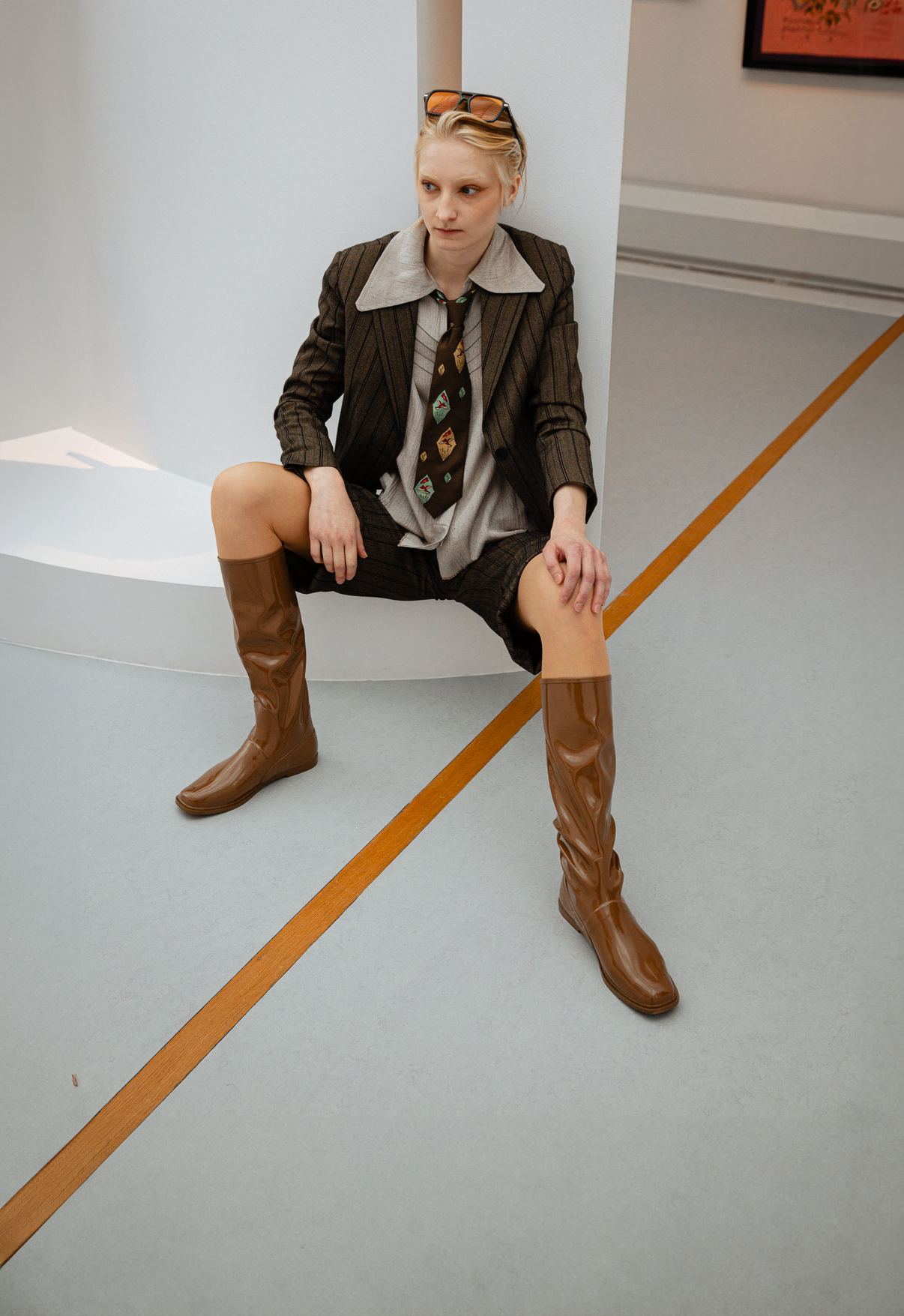 Woman wearing Svea Walnut Brown knee-high boots by ACQUO of Sweden styled with a tailored pinstripe suit and patterned tie in a contemporary studio setting. Waterproof boots with minimalist Swedish design, square toes and an elegant modern silhouette in warm walnut brown