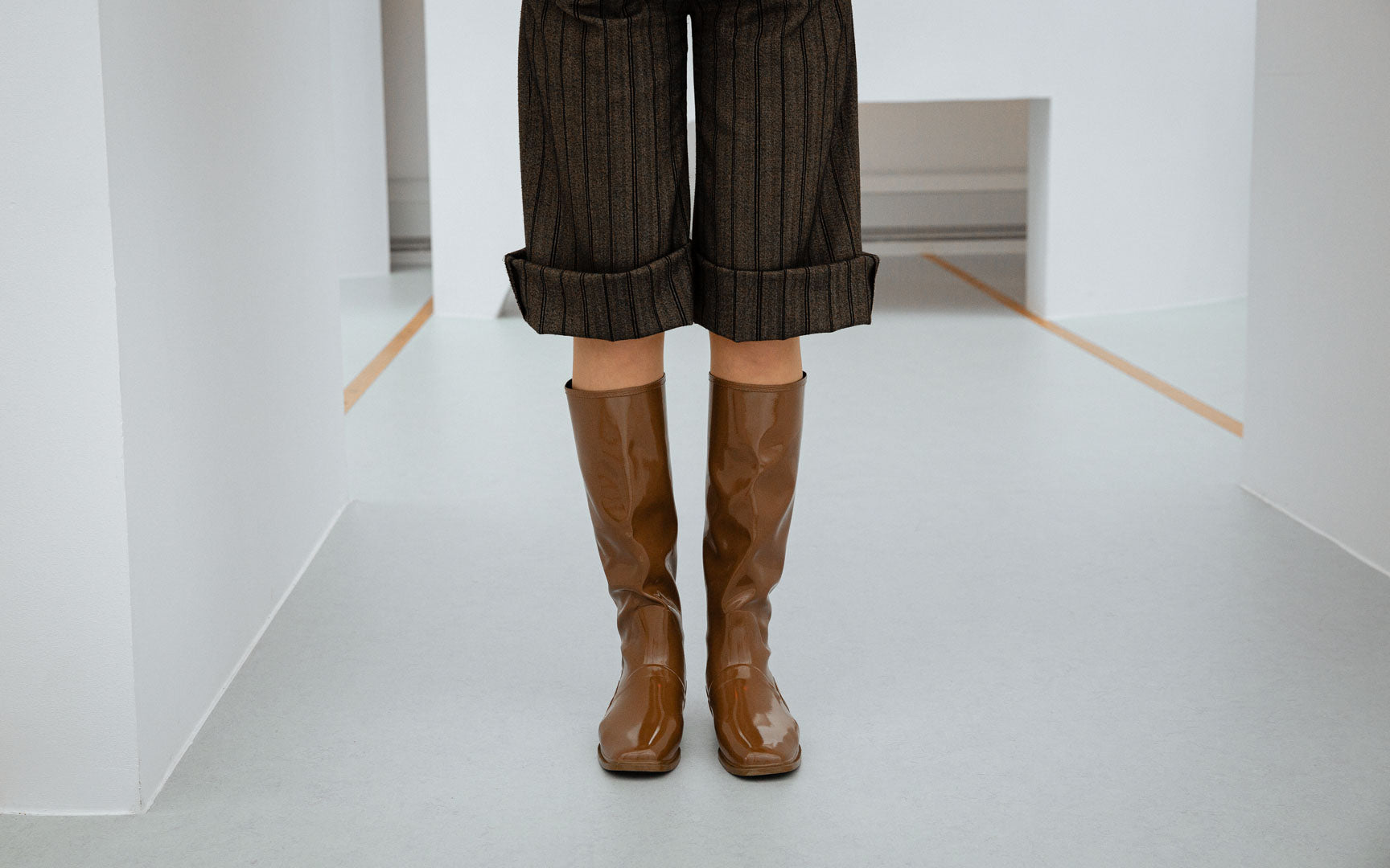 Close-up of ACQUO of Sweden Svea Walnut Brown natural rubber boots, styled with cropped pinstripe trousers in a modern Scandinavian interior