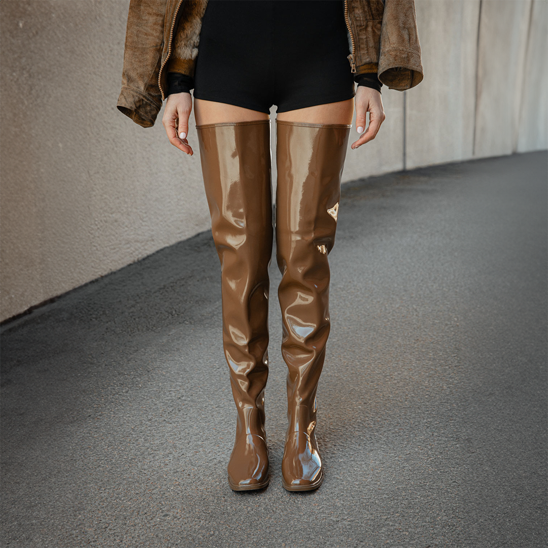 Close-up of Vega Walnut Brown over-the-knee boots by ACQUO of Sweden styled with black shorts and a brown jacket in a modern outdoor setting. Waterproof boots featuring elegant Swedish design and contemporary Scandinavian fashion
