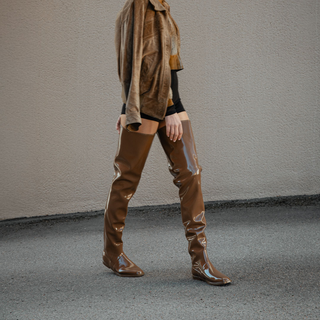 Woman walking in Vega Walnut Brown over-the-knee boots by ACQUO of Sweden styled with black shorts and a brown jacket. Waterproof boots with elegant Swedish design and modern Scandinavian fashion aesthetics