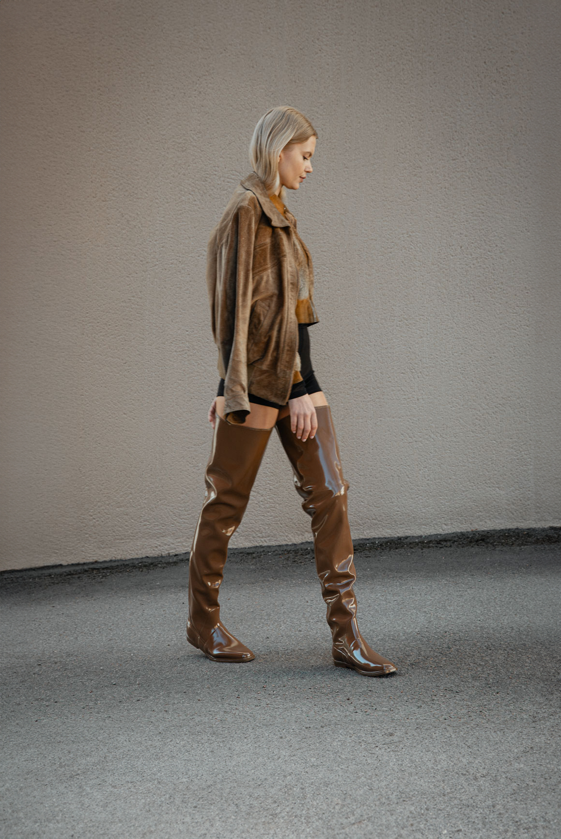 Woman walking in Vega Walnut Brown over-the-knee boots by ACQUO of Sweden styled with black shorts and a brown jacket. Waterproof boots with elegant Swedish design and modern Scandinavian fashion aesthetics